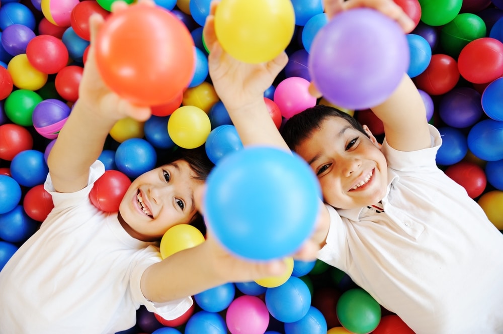 Two smiling boys holding up colourful balls in a ball pit