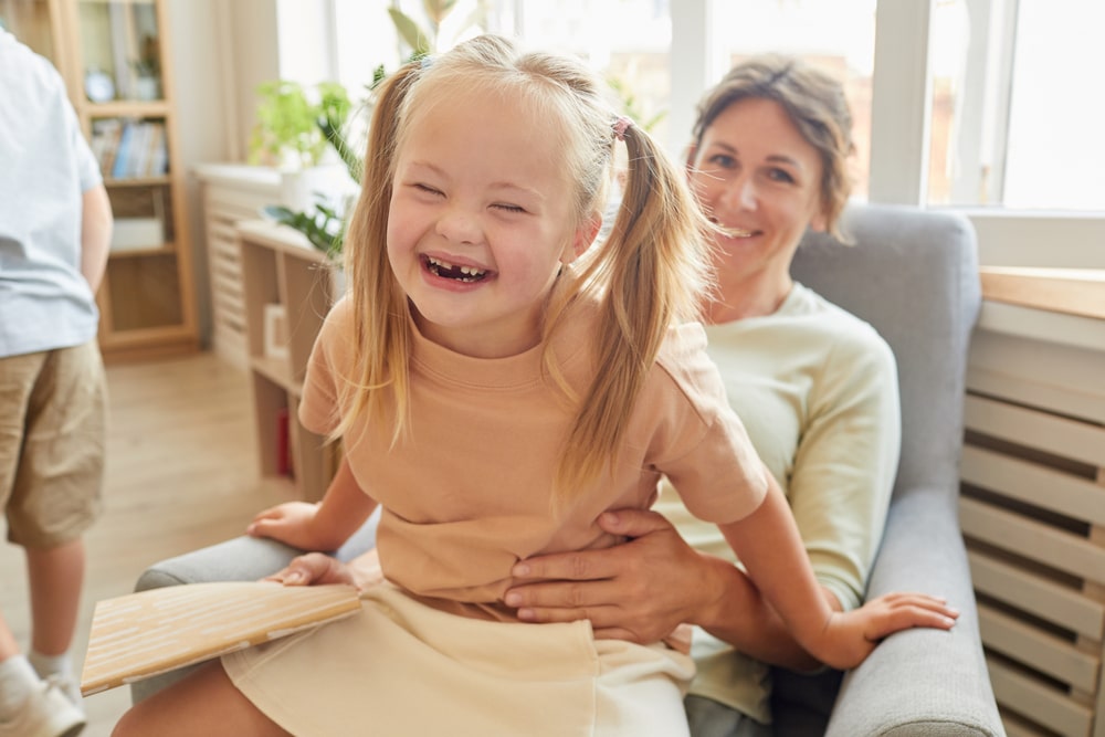 Smiling girl with Down syndrome sitting on her mother's lap at home