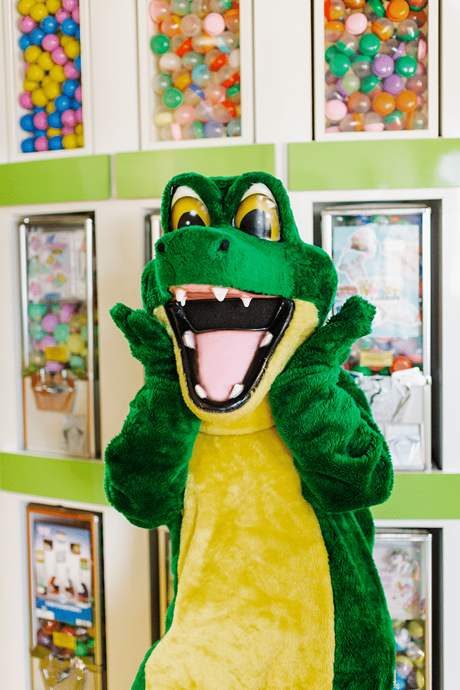 Allie the Alligator, the practice mascot, cheering in front of the office prize-machine wall